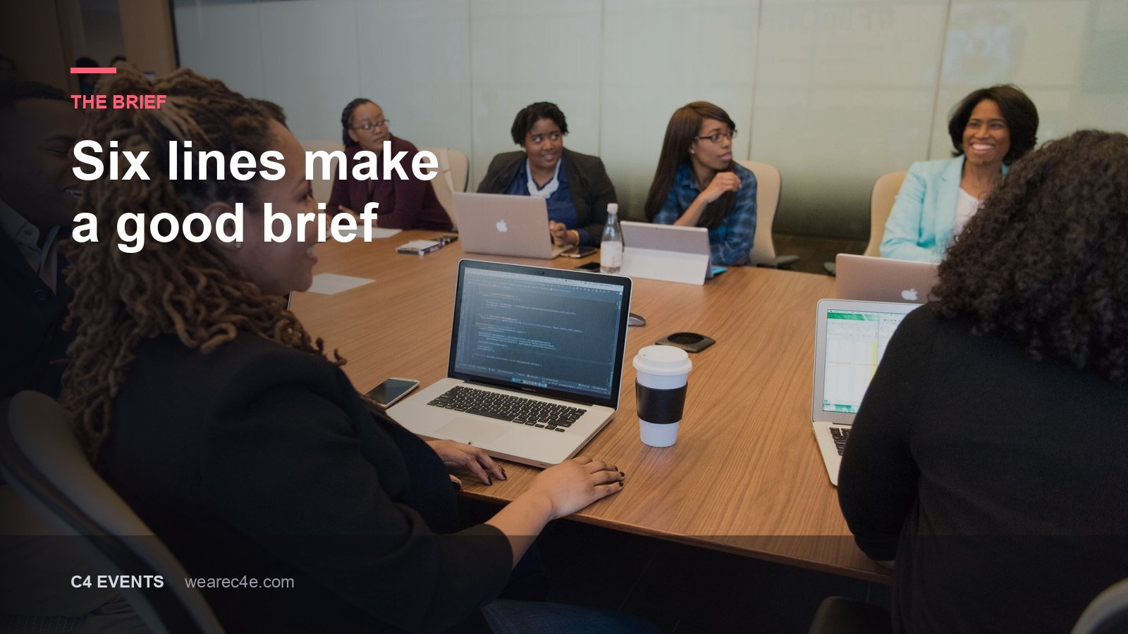 Colleagues around a boardroom table with laptops open, mid-discussion.