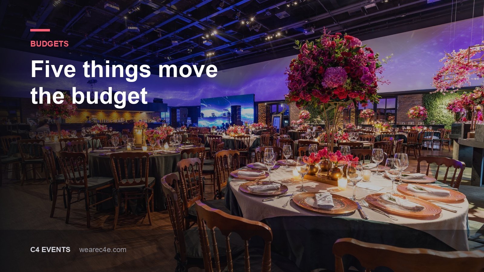 A ballroom laid for a gala dinner, round tables under coloured uplighting.