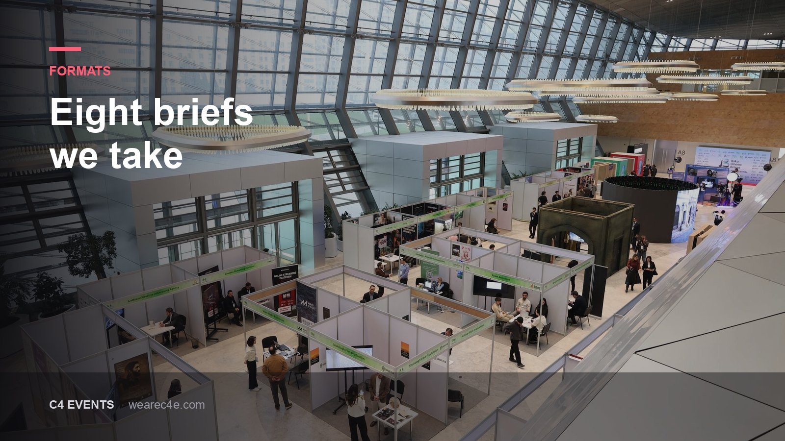 An exhibition floor of stands seen from above inside a glass-roofed hall.