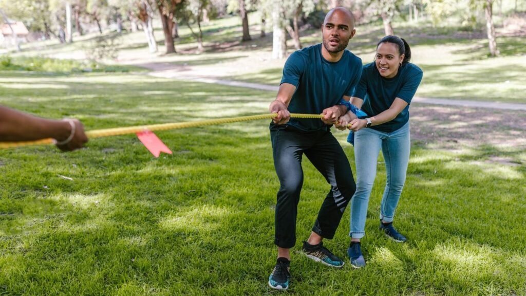 Two adults engaging in a tug of war during a team building event in a park.